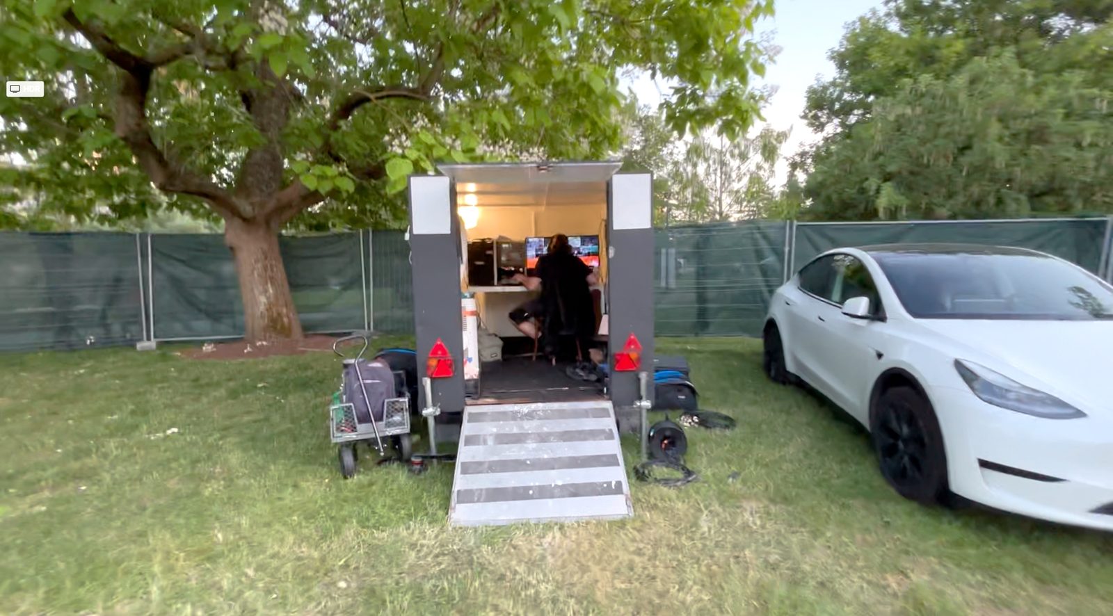 La remorque régie installée au bord d'une pelouse de festival, porte ouverte sur la régie