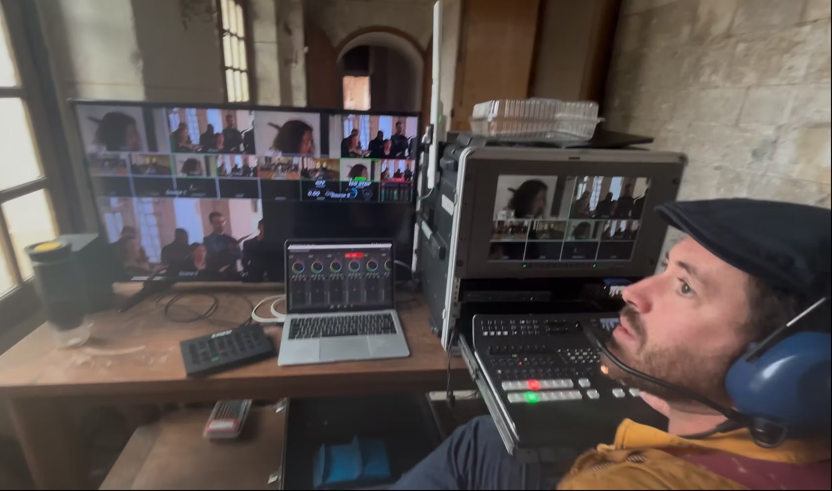 Réalisateur en régie dans une salle aux murs de pierre, casque sur les oreilles, devant le multiview et le mélangeur